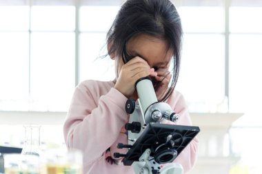 Asyalı çocuklar mikroskobu bilim adamıyla değerlendiriyor. Sağlık araştırmacıları damlatan kimyasallarla ilgili araştırma yapıyor ve yaşam bilimi laboratuvarında çalışıyor.