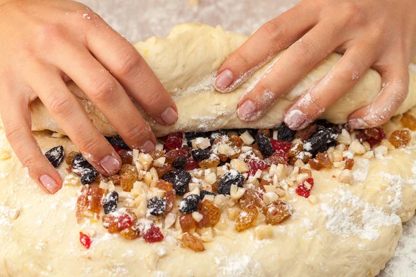 Two hands wrapped candied fruits in dough against the background of a floured table