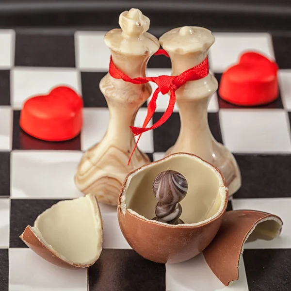 Bir çikolata yumurta çikolata satranç taşları ve siyah ve beyaz hücreleri üzerinde kırmızı kalpler arka planı koyu çikolata piyon