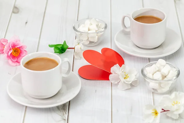 Decorative heart and two cups of coffee with dessert on the background of a light table top and artificial flowers