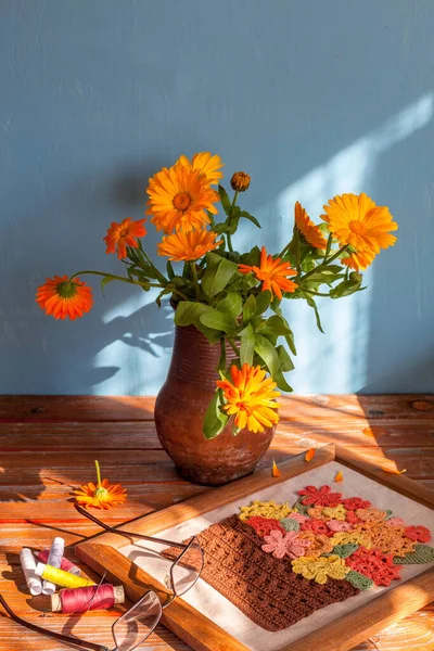 Arka planda mavi bir arka planda eski bir kil saksıda manzaralı bir buket. Önplanda güneş ışığı ve dikiş demeti var.