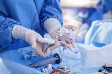 Ortopedi cerrahı, artroplasti hazırlığı sırasında steril kumaşa diz protezi nakli parçaları gösteriyor. Tıp eğitimi ve pazarlama için ideal.