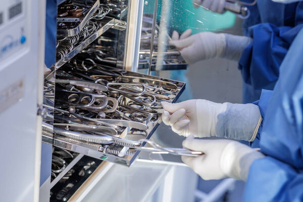 Technician in blue scrubs organizes clean metal tools on racks inside a sterilization cabinet, illustrating aseptic workflow and infection control.
