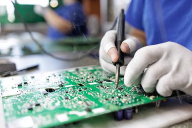 ESD eldivenli işçinin modern bir fabrikadaki elektronik montaj istasyonunda yeşil bir PCB lehimleme parçalarını kapatması.