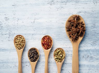 Tahta kaşık, beyaz boyalı masada bitkilerle ve baharatlarla dolu.