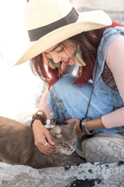 Şapkalı Asyalı kadın sevimli kediyle oynuyor.