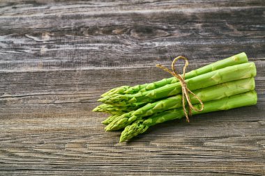 Kuşkonmaz gri bir ahşap zemin üzerine taze yeşil sürgünler. Taze kuşkonmaz demet