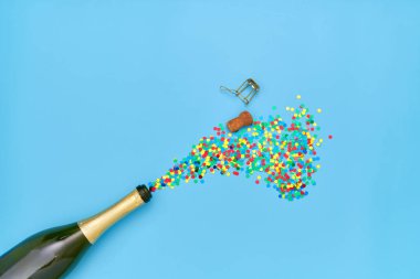 Creative photo of champagne bottle with colorful confetti on blue  background. Flat lay of christmas, anniversary, new year celebration concept clipart