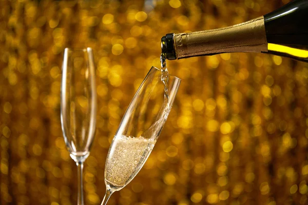 Wylewanie szampana do szklanki na złotym stylowym tle ze złotymi kręgach bokeh miejsce dla tekstu — Zdjęcie stockowe