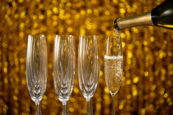 Pouring champagne into glass on golden stylish background