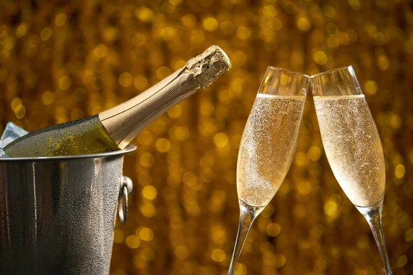 Volle fles Champagne in een emmer met ijs en twee glazen champagne op de gouden bokeh achtergrond — Stockfoto