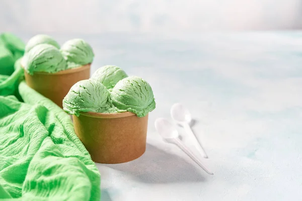 Dos porciones de helado de pistacho en taza de papel y servilleta verde sobre fondo de colores menta, enfoque selectivo — Foto de Stock