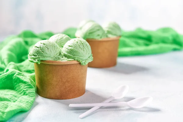 Dos porciones de helado de pistacho en taza de papel y servilleta verde sobre fondo de colores menta, enfoque selectivo — Foto de Stock
