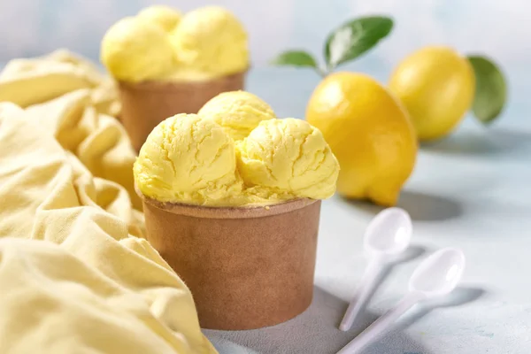 two portions lemon ice cream in paper cup and yellow napkin on mint colors background, selective focus