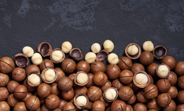 Siyah masa üzerinde kabuklu ve kabuksuz macadamia fındık, kopya alanı ile. Üstte görüntü.