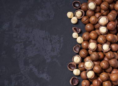Siyah masa üzerinde kabuklu ve kabuksuz macadamia fındık, kopya alanı ile. Üstte görüntü.
