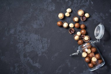 Siyah masa üzerinde açık bir cam kavanozda kabuklu ve kabuksuz macadamia fındık, kopya alanı ile. Üstte görüntü.