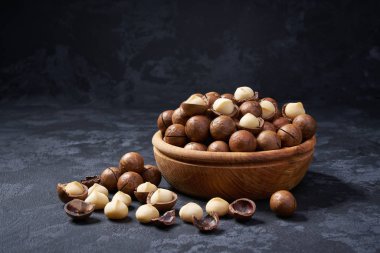 Siyah arka plan üzerinde ahşap kase içinde kabuklu ve kabuksuz macadamia fındık, yakın çekim.