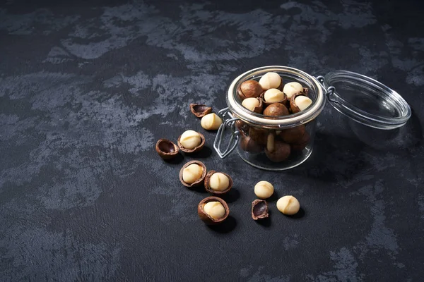 Nueces de macadamia en un frasco de vidrio abierto sobre una mesa negra, con espacio para copiar . — Foto de Stock