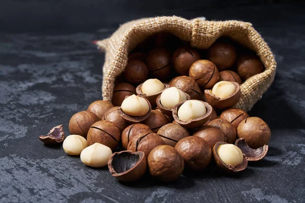Las nueces de macadamia se vierten fuera de la bolsa sobre una mesa negra, de cerca . — Foto de Stock