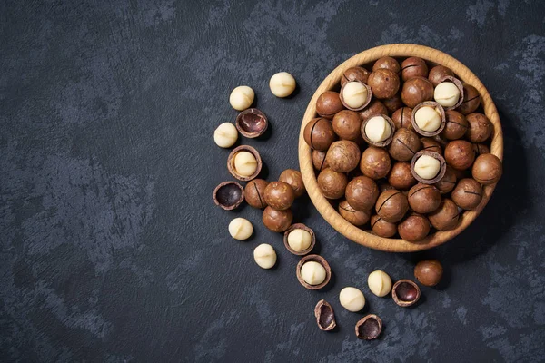 Macadamia nuts  in wooden bowl on black background with copy space. Top view