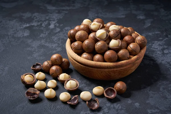 Nueces de macadamia ecológicas en tazón de madera sobre fondo negro, primer plano . — Foto de Stock