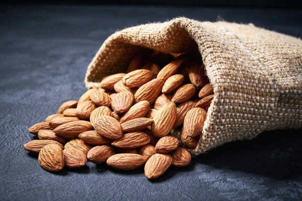 Amandes en sac de toile de jute sur fond noir avec espace de copie — Photo