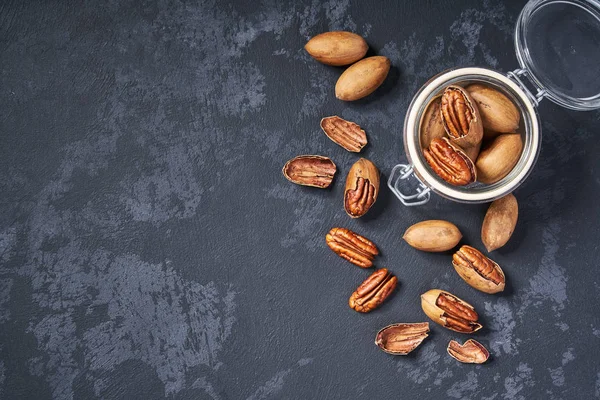 Ekologisk pecan i en glasburk på ett svart bord, med kopierings utrymme. Uppifrån och. — Stockfoto