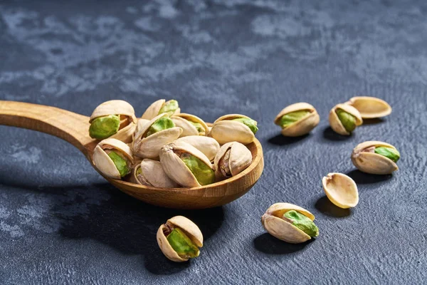 Pistachios in wooden spoon on black table, close-up. — Stock Photo, Image
