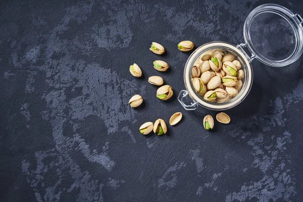 Organic pistachios in a glass jar on an black table, with copy space. Top view. — Stock Photo, Image