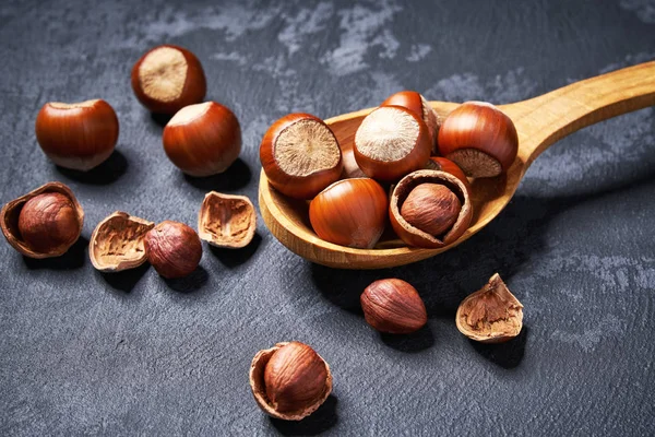 Hazelnut in wooden spoon on black table, close-up. — Stock Photo, Image