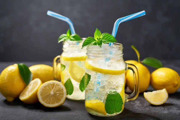 Erfrischende gekühlte Limonade in Gläsern auf schwarzem Hintergrund mit frischer Zitrone. — Stockfoto