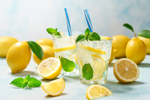 два бокала лимонада со свежим лимоном на бирюзовом фоне
