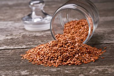 Kırsal bir zemindeki cam bir kavanozdan keten tohumu dökülüyor. Açık cam kavanozda keten tohumu.