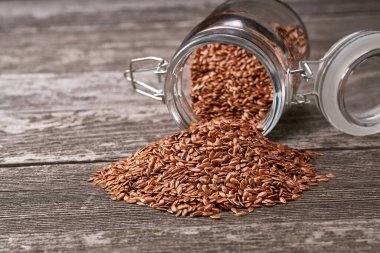 Kırsal bir zemindeki cam bir kavanozdan keten tohumu dökülüyor. Açık cam kavanozda keten tohumu.