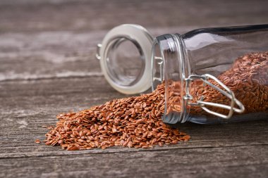 Gri ahşap arka planda cam bir kavanozdan keten tohumları dökülür..