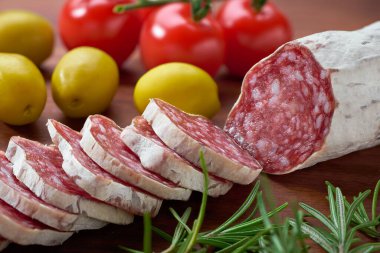 Geleneksel İspanyol Fueti ahşap bir tahtada dilimlenmiş ince sosis zeytin ve biberiyenin yanında.