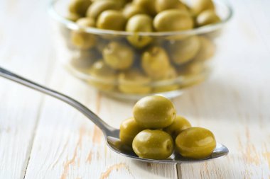 Beyaz mutfak masasında salamura edilmiş yeşil zeytin, seçici bir odak..