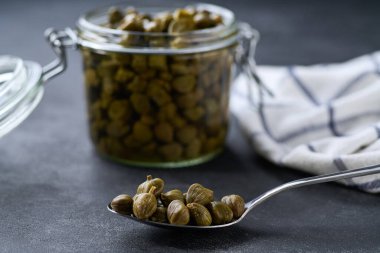 Siyah taş bir masada kavanozda turşu tomurcukları, seçici bir odak noktası..