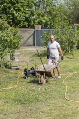 adam iterek el arabası. Genç adam çiftlikte bir el arabası itme.