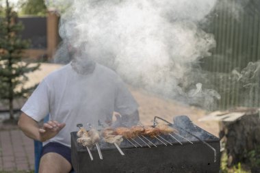Yangın ve ızgara fry et ve sosis yakınındaki bir sakallı bir adam.