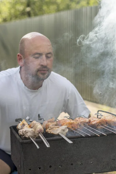 middle-aged man enjoys cooking meat on the grill. leisure, food, people and holidays concept - happy young man cooking meat on barbecue grill at outdoor summer party.