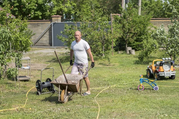 adam iterek el arabası. Genç adam çiftlikte bir el arabası itme