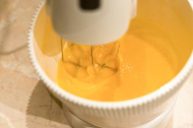 Sarı yumurta sarısı taze kek hamuru modern bir mutfak için dayak Mutfak mikser. Bir açıda açıkça görünür karıştırma çırpma teli ile vurdu.