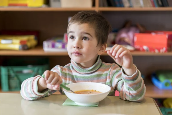 A boy at the age of 4 years eating soup in the kindergarten