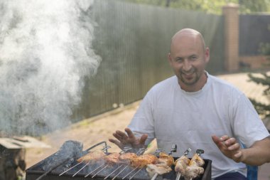 Yangın ve ızgara fry et ve sosis yakınındaki bir sakallı bir adam. Genç bir adam bir Barbekü bir ızgara patates kızartması bir yaz gününde
