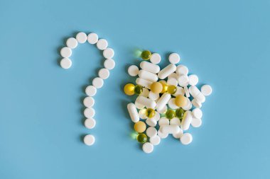 Tıp hap, tablet ve kapsüller sembolü soru işareti mavi bir arka plan üzerinde. Soru işareti olarak mavi zemin üzerine beyaz tabletler.