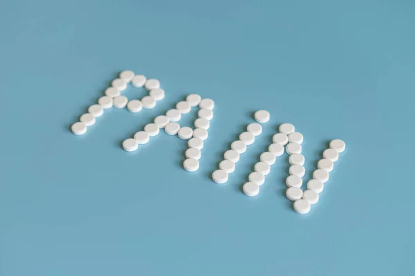 La inscripción del dolor se presenta con pastillas blancas sobre un fondo azul. Control del dolor - Tabletas . — Foto de Stock