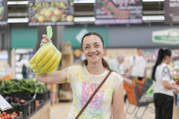 Happy girl bought bananas in the store. Smiling woman with bananas in hand. Blurry