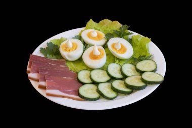 Kahvaltı. Haşlanmış yumurta, pastırma, izole bir siyah arka plan üzerine beyaz bir tabak içinde Yeşiller.